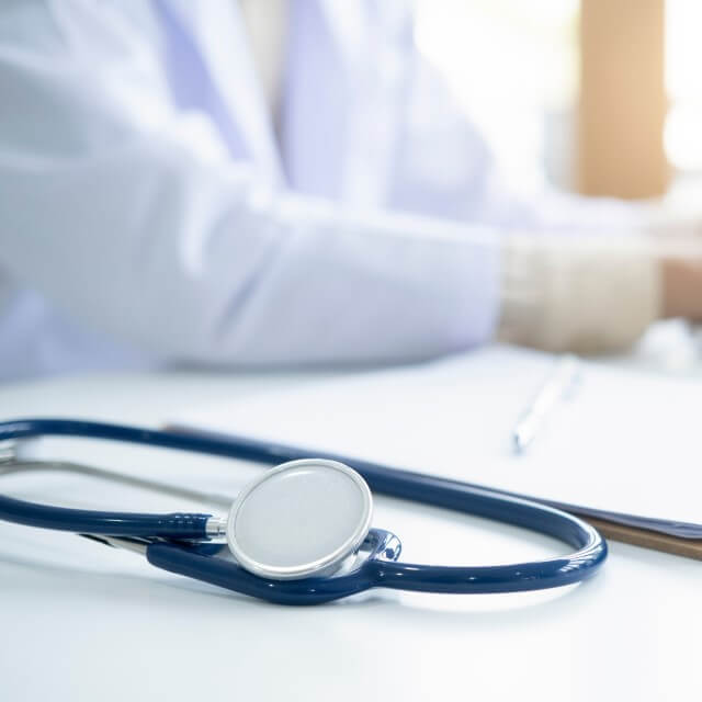 Stethoscope in focus in the foreground with white suited gentleman blurry in background